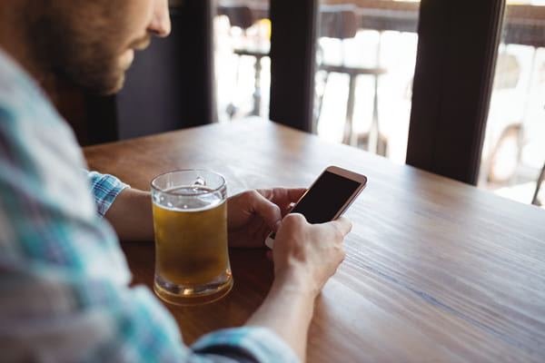 mężczyzna siedzący przy barze korzysta z telefonu a pomiędzy rękoma znajduje się szklanka z bezalkoholowym piwem