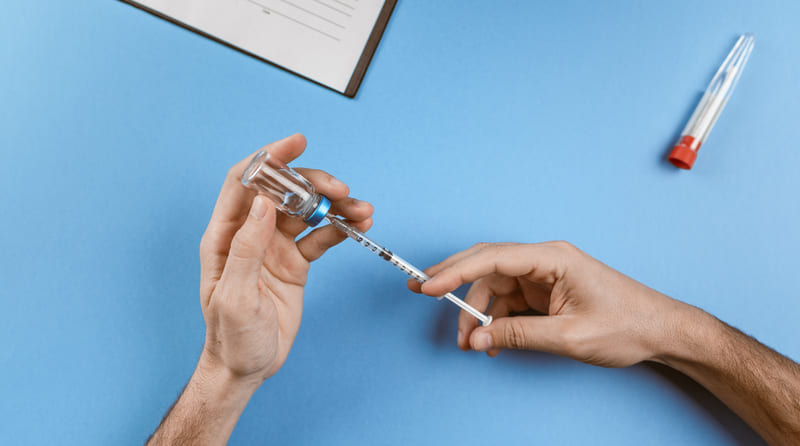 Lekarz pobiera szczepionkę do strzykawki z ampułki na niebieskim blacie
